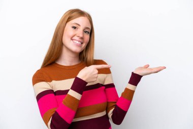 Beyaz arka planda izole edilmiş genç, kızıl saçlı bir kadın. Bir ilan vermek için avucunda hayali bir şey tutuyor.