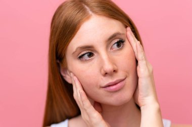 Genç kızıl saçlı kadın pembe arka planda izole edilmiş.