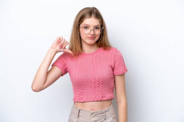 Beyaz arka planda izole edilmiş genç bir Rus kızı, olumsuz ifadeyle baş parmağını aşağı gösteriyor.