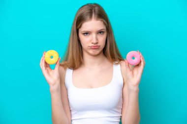 Genç Rus kız mavi arka planda izole edilmiş elinde üzgün bir ifadeyle donut tutuyor.