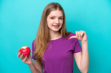 Mavi arka planda olgun elma tutan genç kız.