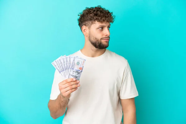 Jonge Kaukasische Man Neemt Veel Geld Geïsoleerd Blauwe Achtergrond Kijken — Stockfoto