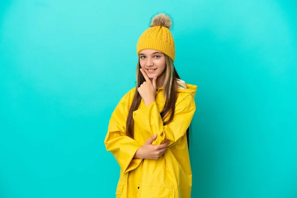 穿着防雨外套的小女孩在孤零零的蓝色背景上快乐地微笑着 — 图库照片