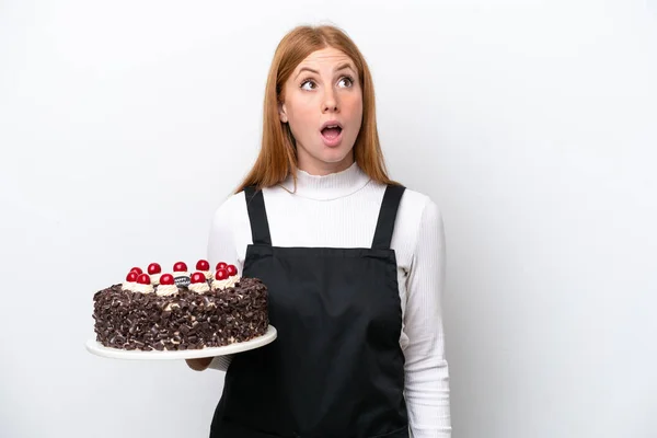 若いです赤毛女性保持誕生日ケーキ隔離された上を見ますととともに驚きの表情 — ストック写真