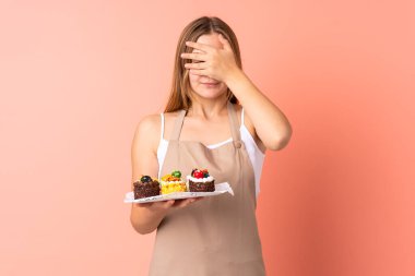 Ukraynalı aşçı, pembe arka planda gözlerden izole edilmiş bir kek tutuyor.