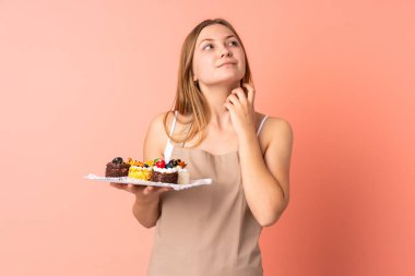 Ukraynalı aşçı pembe arka planda izole edilmiş bir kek tutarak bir fikir düşünüyor.