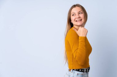 Mavi arka planda izole edilmiş genç Ukraynalı kız bir ürünü sunmak için kenarı işaret ediyor