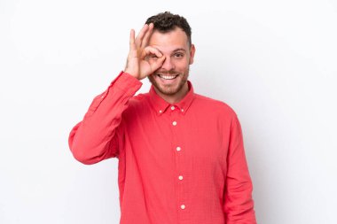 Beyaz arka planda izole edilmiş genç Brezilyalı adam parmaklarıyla tamam işareti gösteriyor