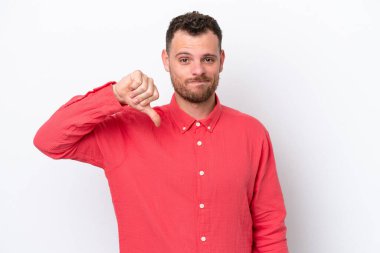 Beyaz arka planda izole edilmiş genç Brezilyalı adam olumsuz ifadeyle baş parmağını aşağı gösteriyor.