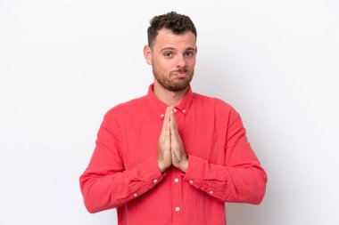 Beyaz arka planda izole edilmiş genç Brezilyalı adam avuç içlerini bir arada tutuyor. İnsan bir şey ister.