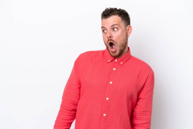 Beyaz arka planda izole edilmiş genç Brezilyalı adam yan tarafa bakarken sürpriz jest yapıyor.