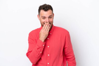 Genç Brezilyalı bir adam beyaz arka planda izole edilmiş mutlu ve gülümseyen ağızlarını eliyle kapatıyor.