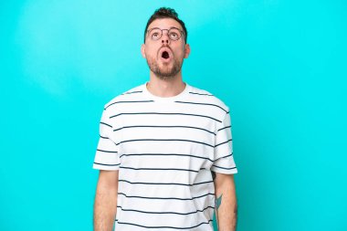 Genç Brezilyalı adam mavi arka planda izole edilmiş yukarı bakıyor ve şaşırmış bir ifadeyle