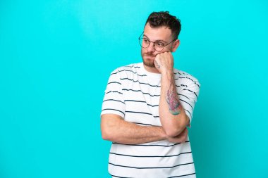 Genç Brezilyalı adam mavi arka planda izole edilmiş, yorgun ve sıkılmış bir ifadeyle.