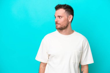 Mavi arka planda izole edilmiş genç Brezilyalı adam yan tarafa bakıyor.