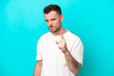 Genç Brezilyalı adam mavi arka planda izole edilmiş hayal kırıklığına uğramış ve ön tarafı işaret ediyor.