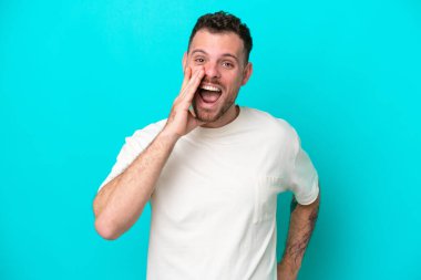 Mavi arka planda izole edilmiş genç Brezilyalı adam ağzı açık bağırıyor.