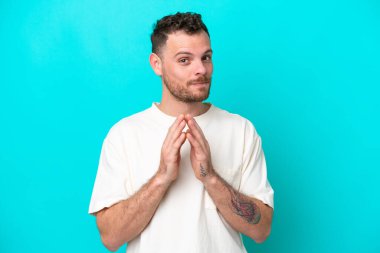 Genç Brezilyalı bir adam mavi arka planda bir şeyler planlıyor.