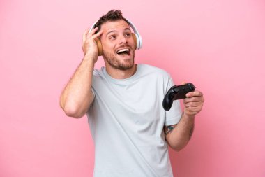 Pembe arka planda izole edilmiş bilgisayar oyunu kontrolörüyle oynayan Brezilyalı genç adam çok gülümsüyor.