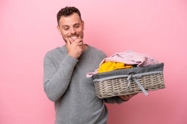 Genç Brezilyalı bir adam pembe arka planda izole edilmiş bir sepet tutuyor. Yan tarafa bakıyor ve gülümsüyor.