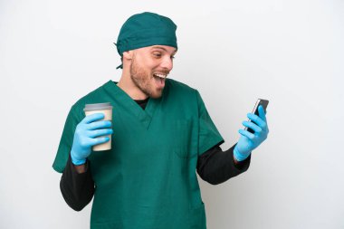 Cerrah Brezilyalı yeşil üniformalı adam beyaz arka planda izole edilmiş. Elinde kahve ve cep telefonu var.