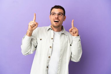 İzole edilmiş mor arka planı olan Brezilyalı adam şaşırmış ve yukarı bakıyor.