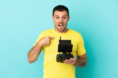 Brezilyalı bir adam uzaktan kumandayla izole edilmiş mavi arkaplan üzerinde sürpriz yüz ifadesiyle