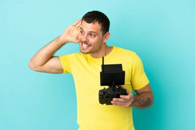 Brezilyalı bir adam uzaktan kumandayla izole edilmiş mavi arkaplanı kontrol ediyor. Kulağına elini koyarak bir şey dinliyor.