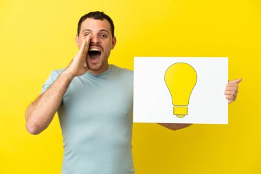 İzole edilmiş mor arka plan üzerinde Brezilyalı bir adam elinde ampul simgesi olan bir levha tutuyor ve bağırıyor: