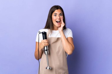 Mor zemin üzerinde el blenderi kullanan Brezilyalı kadın şaşırmış ve şok olmuş yüz ifadesi takınıyor.