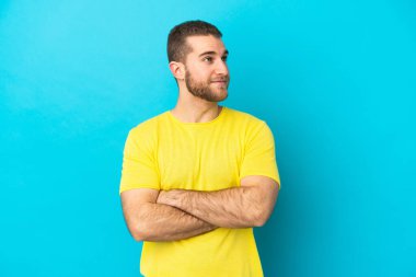 Mavi arka planda izole edilmiş yakışıklı beyaz adam yan tarafa bakıyor.