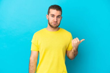 Mavi arka planda izole edilmiş yakışıklı beyaz adam mutsuzdu ve yüzünü gösteriyordu.