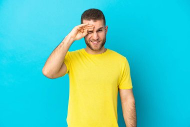 Genç, yakışıklı, beyaz bir adam mavi arka planda izole edilmiş, yorgun ve hasta bir ifadesi var.