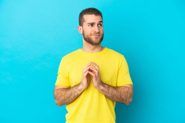 Genç yakışıklı beyaz adam, mavi arka planda izole edilmiş bir şekilde bir şeyler planlıyor.