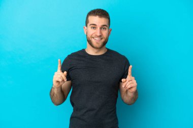 Mavi arka planda izole edilmiş yakışıklı beyaz adam harika bir fikre işaret ediyor.
