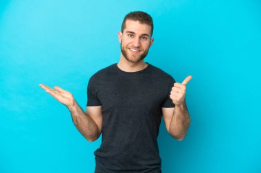 Genç, beyaz, mavi arka planda izole edilmiş bir adam. Kopyalama alanı hayali bir şey tutuyor. Bir ilan vermek için.