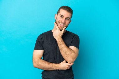 Mavi arka planda izole edilmiş yakışıklı beyaz adam mutlu ve gülümsüyor.