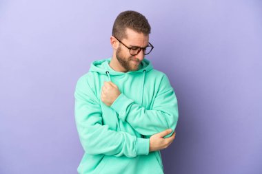 Mor arka planda izole edilmiş, dirsek ağrısı olan yakışıklı beyaz bir adam.