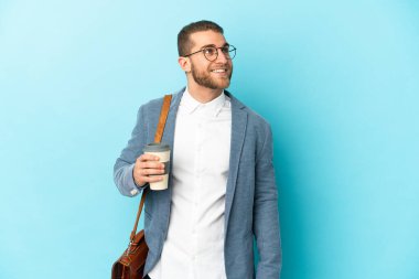 Kafkasyalı genç işadamı mavi arka planda izole edilmiş bir şekilde yukarı bakarken bir fikir düşünüyor.