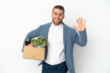 Beyaz arka planda izole edilmiş eşyalarla dolu bir kutuyu alıp mutlu bir ifadeyle selamlayarak hareket eden genç beyaz tenli.