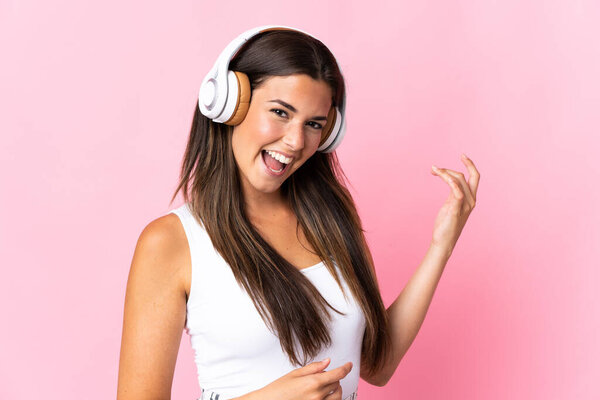 Young brazilian girl isolated on pink background listening music and doing guitar gesture