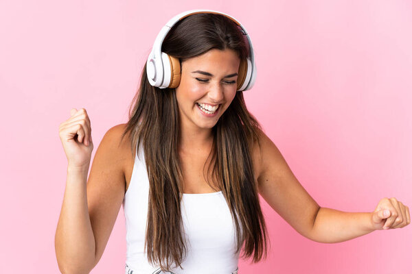Young brazilian girl isolated on pink background listening music and dancing