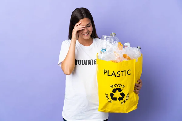 若いブラジル人女性の袋のビニールボトルの袋を保持する紫色の背景に笑って孤立リサイクルする — ストック写真