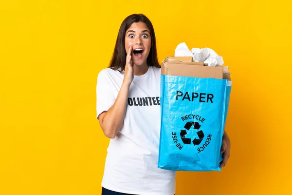 若いですブラジルの女の子を保持していますリサイクルバッグフル紙でリサイクルする黄色の背景に隔離されました驚きとショックを受けた顔の表情 — ストック写真
