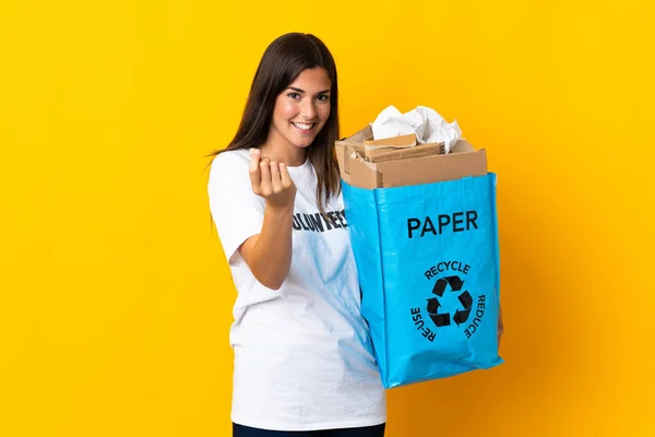 若いですブラジル人の女の子を保持リサイクルバッグフル紙でリサイクルする黄色の背景に隔離されたお金のジェスチャーを作る — ストック写真