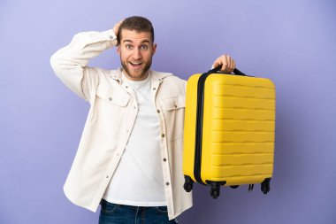 Mor arka planda izole edilmiş, seyahat valiziyle gezen yakışıklı beyaz bir adam.