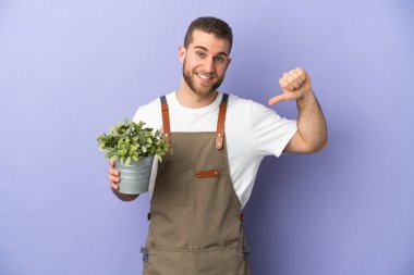 Bahçıvan beyaz adam sarı arka planda bir bitki tutuyor gururlu ve kendinden memnun.