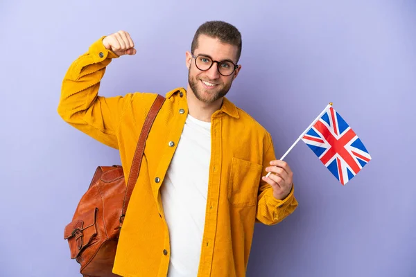 年轻的高加索男子举着英国国旗 背景为紫色 做着强有力的手势 — 图库照片