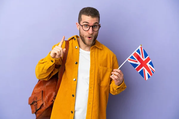 年轻的高加索人拿着一面英国国旗 与紫色背景隔离 想在举手表决的同时实现这个解决方案 — 图库照片