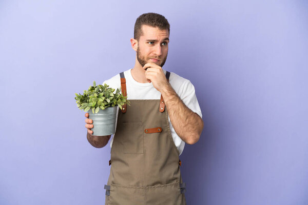 Gardener caucasian man holding a plant isolated on yellow background having doubts and thinking